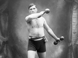 An old photograph capturing a man confidently holding a pair of dumbbells, indicating his dedication to full workouts.