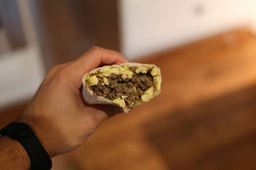 A person holding up a burrito with meat and eggs, perfect for saving time or make-ahead meals.