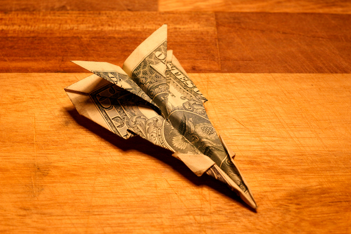 An origami paper airplane, inspired by a fighter jet, resting on a wooden table.