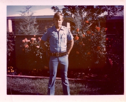 A Game Warden in a police uniform standing in front of flowers.