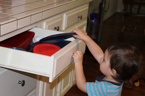 Young boy doing chores putting dishes away kitchen. 
