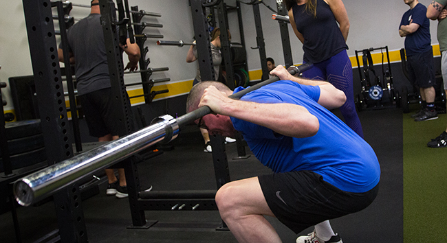A man with low bar squirt in a gym.