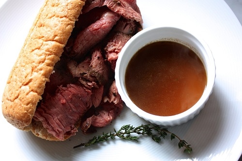 A homemade roast beef sandwich with au jus on a white plate.