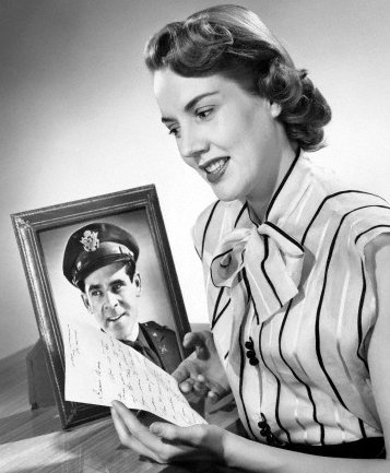 A woman gazes affectionately at a picture of a man in uniform, immersed in the romance it represents.