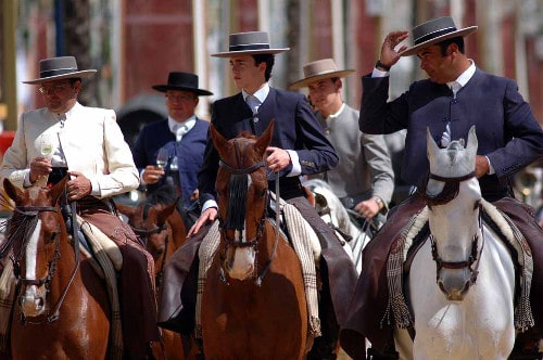 Men in straight brim fedoras and suits riding horses.