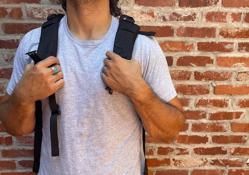 A man with the best backpack stands in front of a brick wall.