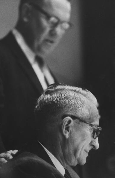 A man in a suit and tie is sitting next to a man in a suit, giving him praise.