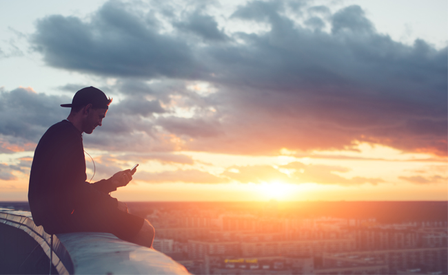 A man sitting on a ledge, quietly observing the sunset.