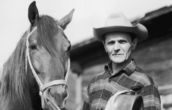 A real man in a cowboy hat standing next to a horse.